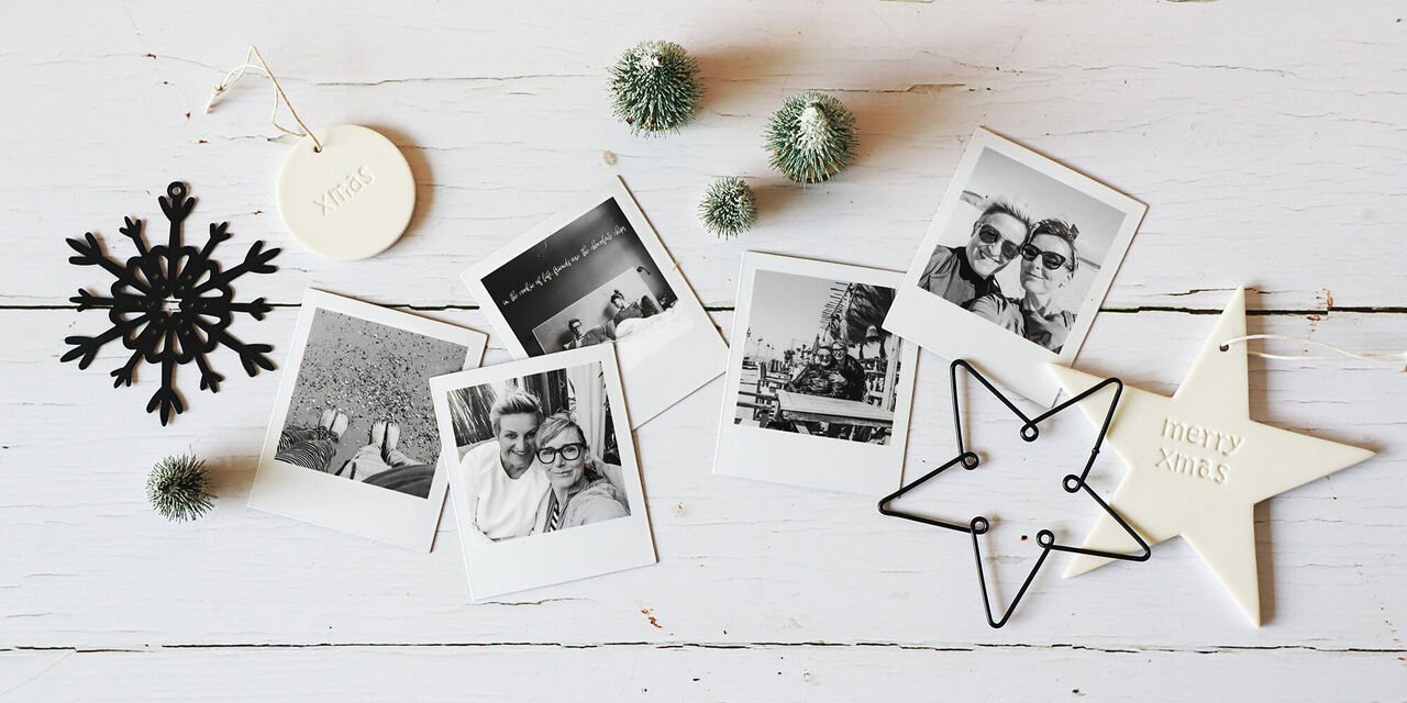 Su un tavolo ci sono diversi magneti con foto in bianco e nero di due amici in vacanza. Intorno a loro ci sono alcune etichette natalizie, anch'esse in bianco e nero.